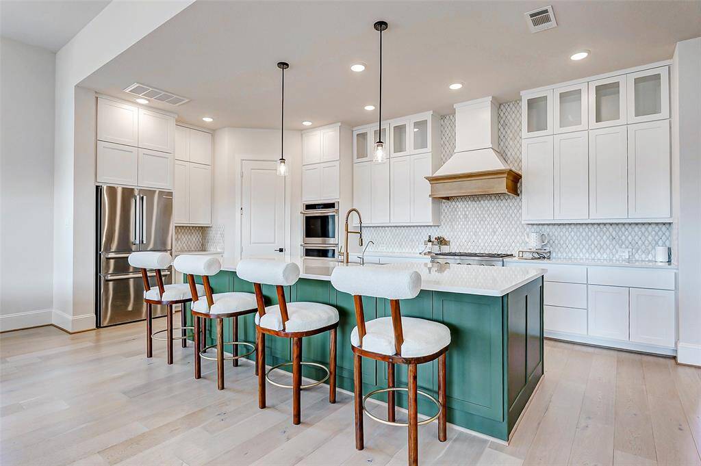 Just beyond the entryway, the heart of the home unfolds in this breathtaking kitchen, designed with an expansive open layout perfect for entertaining. The extended island provides abundant workspace and seating, while cabinets extending to the ceiling, featuring glass inserts in the top row, add a seamless, designer touch.