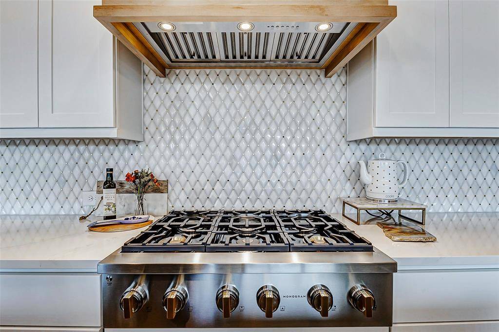A closer look at the stunning 6-burner gas rangetop reveals a beautiful two-tone design of gold and stainless steel. The exquisite backsplash, featuring a diamond pattern with subtle gold accents, adds a refined touch of elegance to the space.