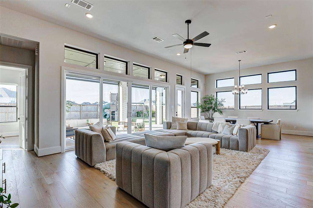 Back inside, take in the abundance of stunning windows that flood the space with natural light. Additional features include upgraded wide plank hardwood floors, recessed lighting, and a modern ceiling fan. This view also reveals the convenient location of the primary suite just beyond.