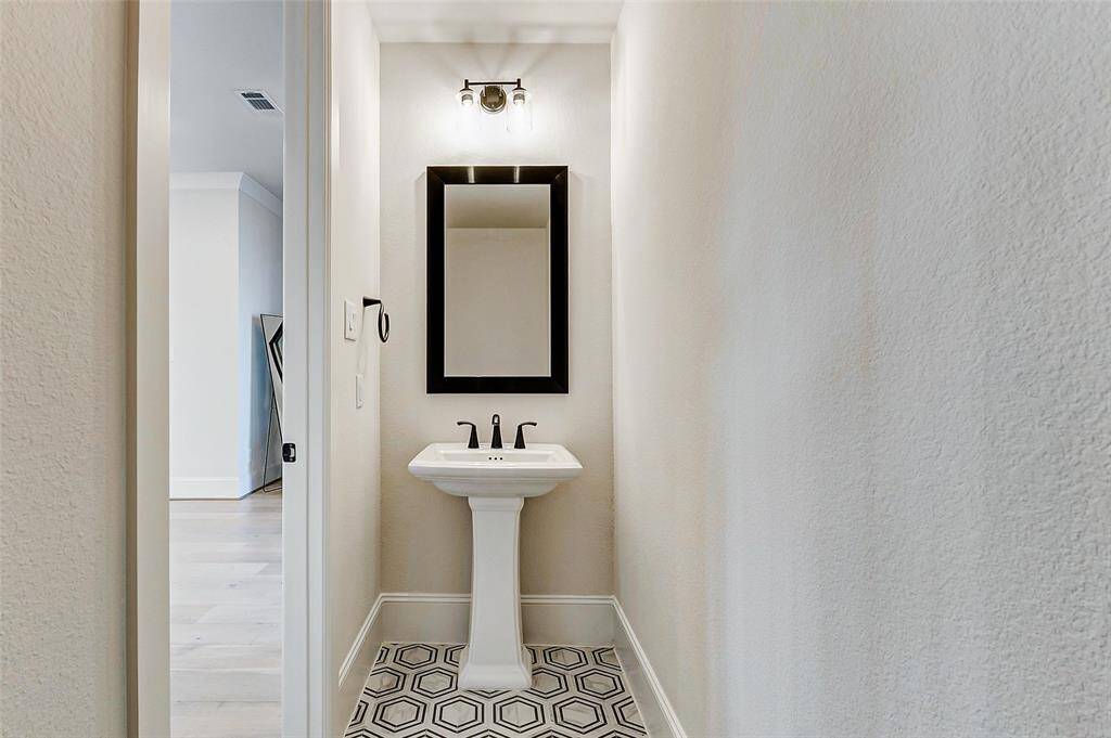 Conveniently located near the entryway, the powder bathroom offers timeless elegance with a beautiful pedestal sink, framed mirror, and stylish lighting fixture. Designer paint, thick baseboards, and accent tile add a refined finishing touch to this charming space.