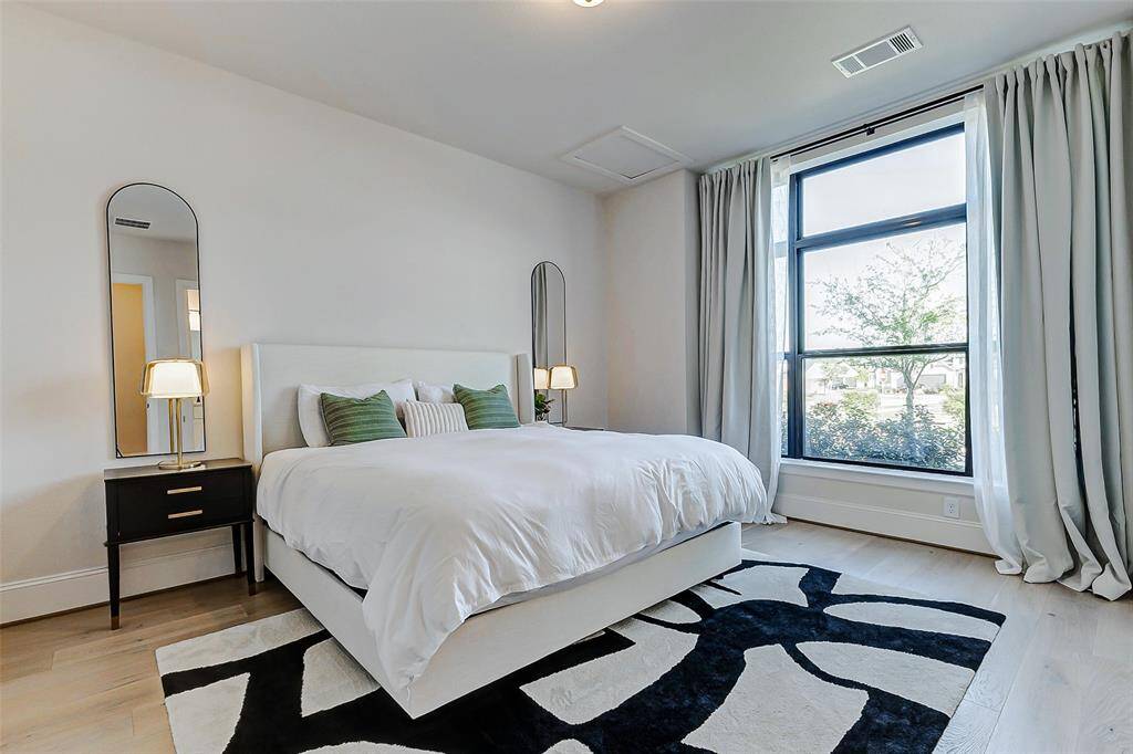 The downstairs guest bedroom offers warmth and charm, highlighted by a striking picture window that draws in natural light and frames views of the front yard. Enhanced by rich hardwood floors, thick baseboards, and designer paint, this space effortlessly blends comfort with elegance.