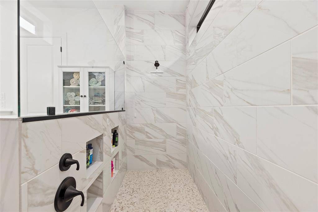 The expansive walk-in shower, adorned with stunning tile work and a sleek glass front, offers a luxurious escape for a quick rinse or a refreshing retreat.