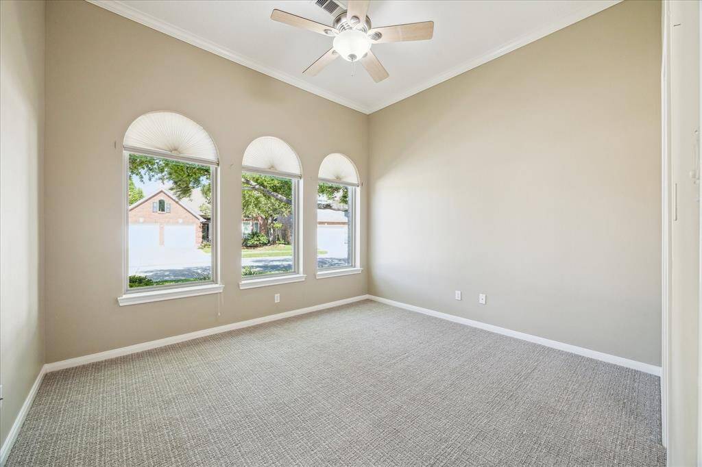 Bright room with high ceilings, soft beige walls, and neutral carpeting. Features three arched windows with a view of the street, providing plenty of natural light. A ceiling fan adds comfort. This bedroom has its own full bathroom making it perfect for guests.