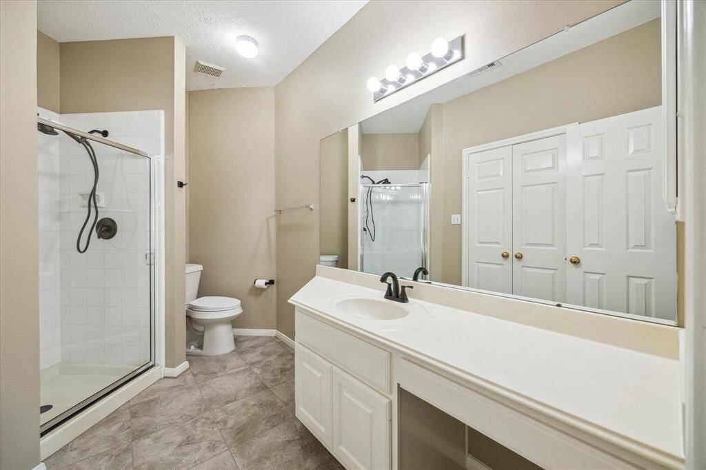 This modern bathroom features a spacious walk-in shower, a sleek single-sink vanity, and abundant lighting throughout. A neutral color palette and a large mirror enhance the sense of space and brightness, creating a clean, open, and inviting atmosphere. Through the double doors is a walk-in closet.