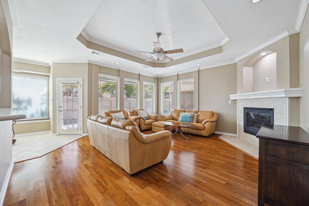 This inviting living room features wood-like laminate floors, a cozy gaslog fireplace, and ample natural light from multiple large windows. It features a neutral color palette, creating a warm and welcoming atmosphere.