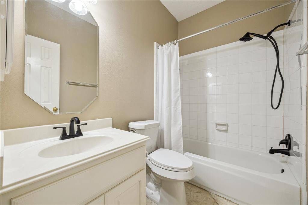 This bathroom features a clean design with a white vanity, modern black fixtures, and a tiled shower-tub combo. The neutral walls and ample lighting create a bright, inviting space.