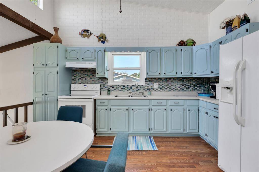 The kitchen's high ceilings are accentuated by a clerestory window, flooding the space with even more natural light. Light blue cabinets paired with crisp white walls and ceilings create a breezy, lakehouse-meets-beach cottage feel, perfectly complemented by the warmth of the wood-look flooring.