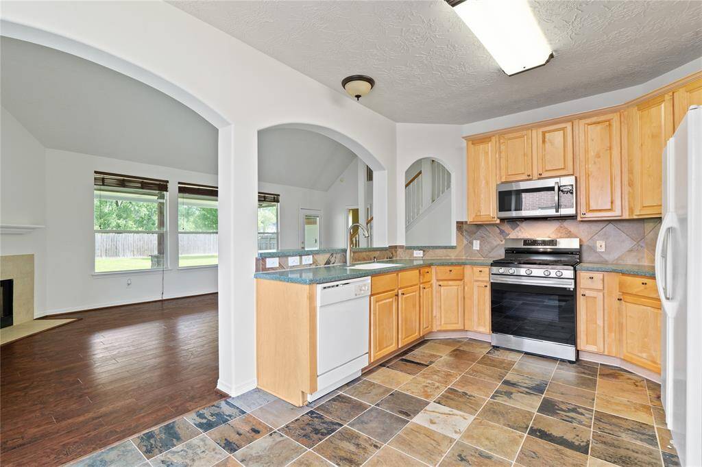 Open concept kitchen with bright countertops, multicolored slate tile, ample cabinet space, and seamless flow into the breakfast area.