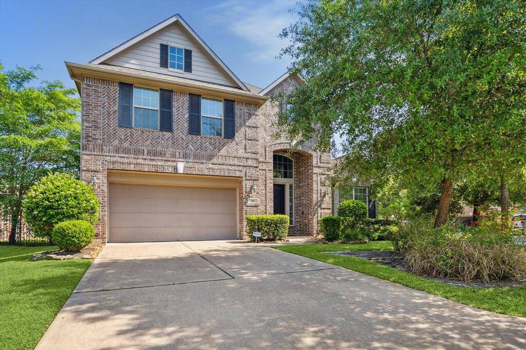 Charming two-story brick home with a spacious two-car garage, surrounded by lush greenery and well-maintained landscaping. The entrance features a welcoming pathway and large windows, providing ample natural light. Perfect for comfortable family living.