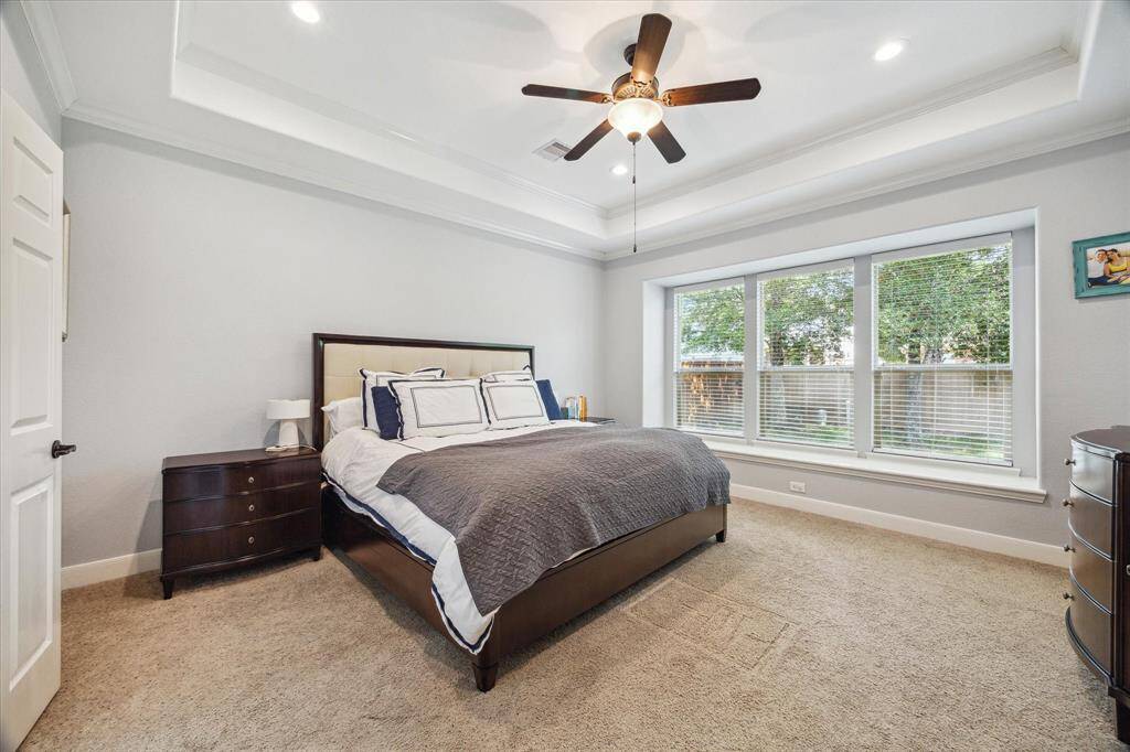 This primary bedroom features a cozy layout with a king-sized bed, neutral carpet, and large windows offering plenty of natural light. It includes a ceiling fan and modern recessed lighting, creating a comfortable and inviting space.