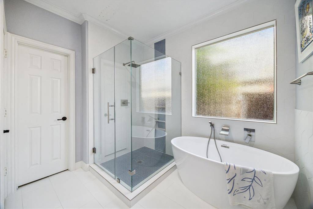 This modern bathroom features a spacious glass-enclosed shower, a sleek freestanding bathtub, and a large frosted window for natural light and privacy.