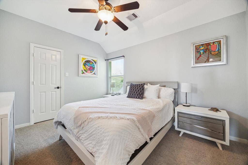 This bright and inviting bedroom features neutral tones, a ceiling fan, and ample natural light.