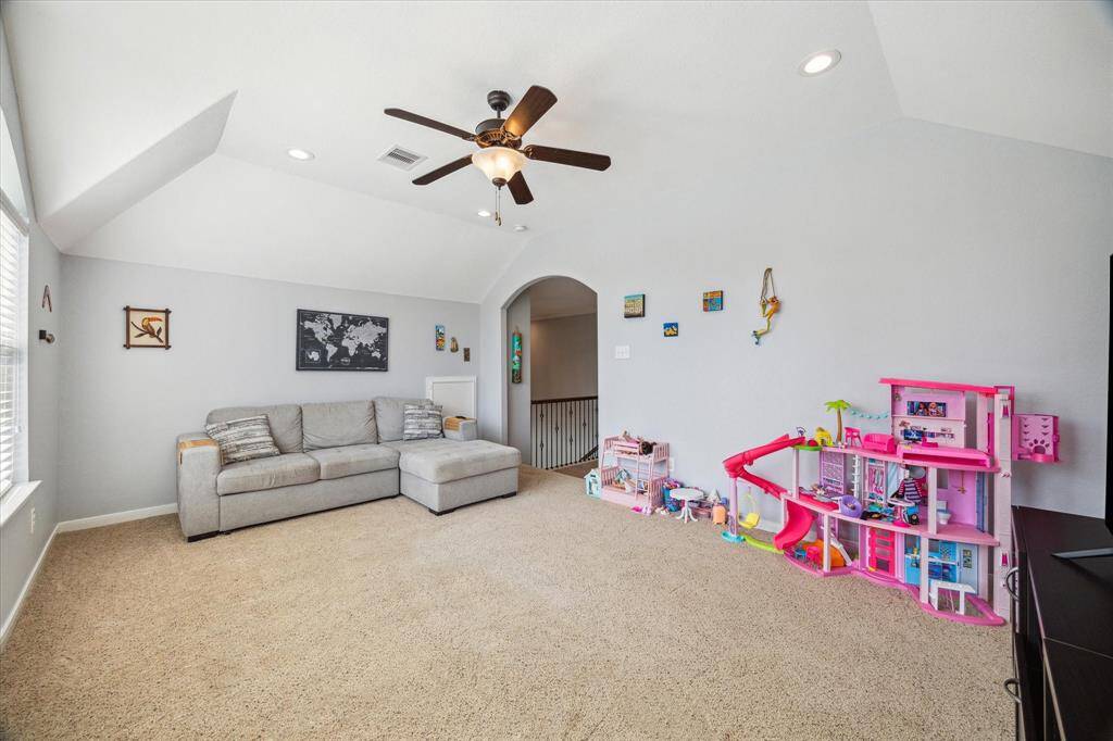 This spacious game room located at the top of the stairs  features neutral carpet, and a ceiling fan. A play area while large windows allow natural light to brighten the space.