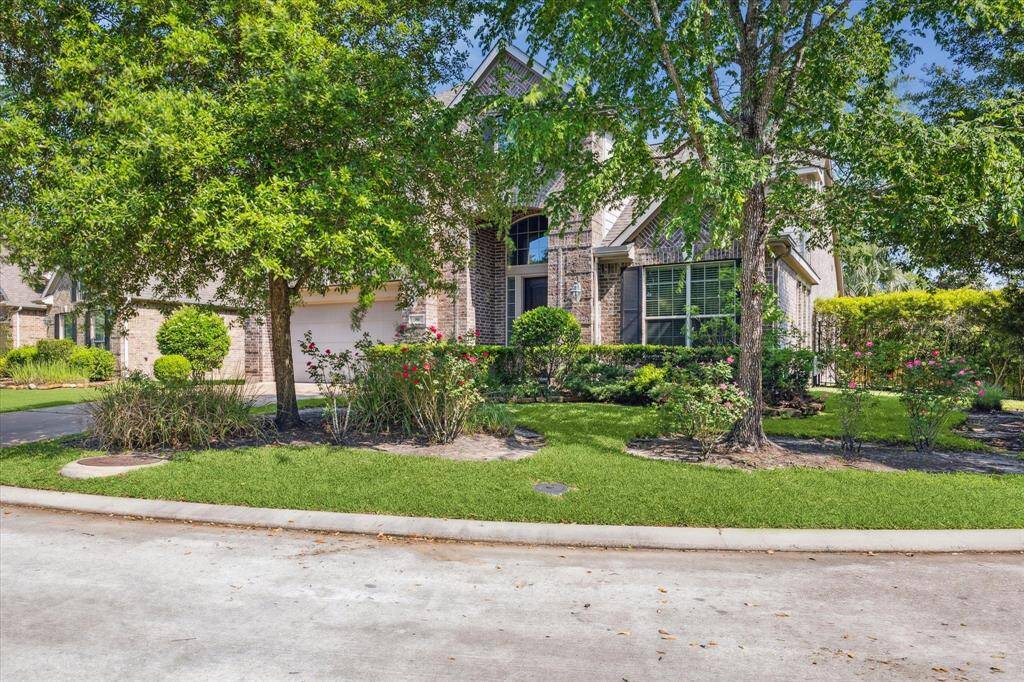 This photo showcases a charming brick home with a well-maintained front yard, featuring lush greenery and mature trees. The house has a welcoming entrance and a two-car garage, set on a quiet street on a corner lot.