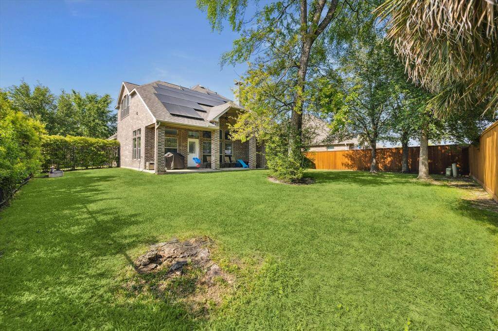 Charming two-story home with solar panels, featuring a spacious, lush backyard lined with mature trees and a wooden privacy fence, perfect for outdoor activities and relaxation.