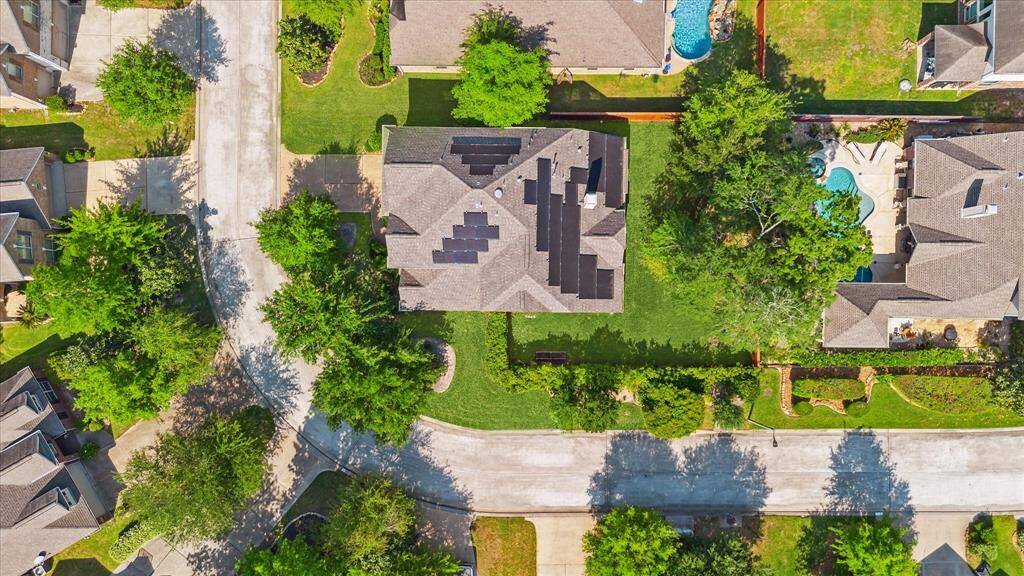 This aerial photo showcases a suburban neighborhood with well-maintained homes, tree-lined streets, and spacious yards. The central house features solar panels on the roof.
