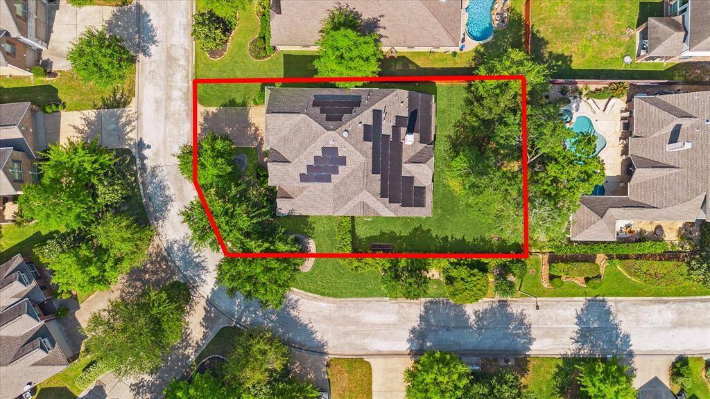 This aerial photo shows a house with a spacious yard outlined in red. It features solar panels on the roof, surrounded by greenery and neighboring homes. The location offers a suburban feel with nearby amenities.