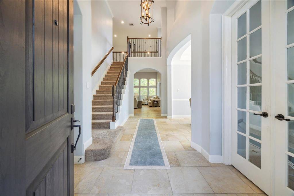 A welcoming foyer with high ceilings, natural light, and a grand staircase. The space features elegant tile flooring, a chandelier, and new front door leading to additional rooms, creating a spacious and inviting entrance.