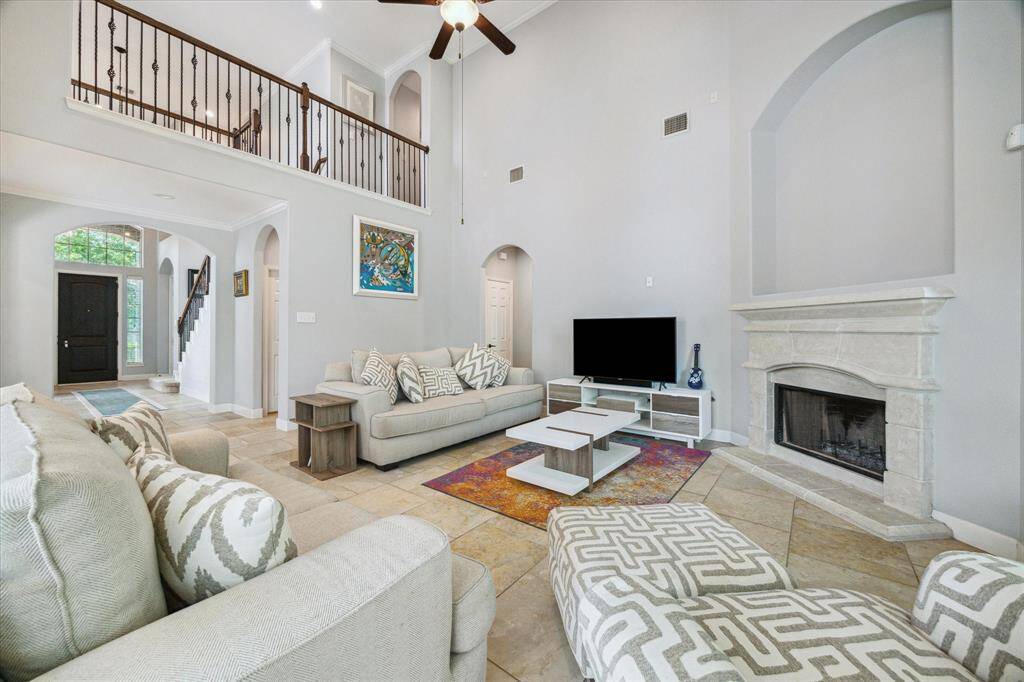Spacious living room with high ceilings, neutral colors, and a stone fireplace. There's an open view to the staircase and front entrance, enhancing the airy feel.