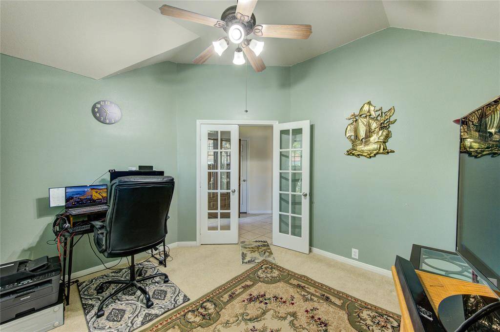 Step through the elegant French doors into a spacious home office, featuring a striking angled ceiling and a wall of windows that fill the room with natural light.