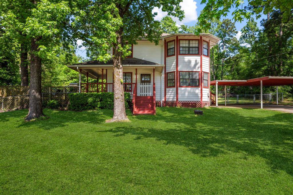 Charming two-story home with a unique turret design, nestled in a lush, green setting. Features a spacious porch, vibrant red accents, and a large carport. Ideal for those seeking a blend of character and outdoor space.