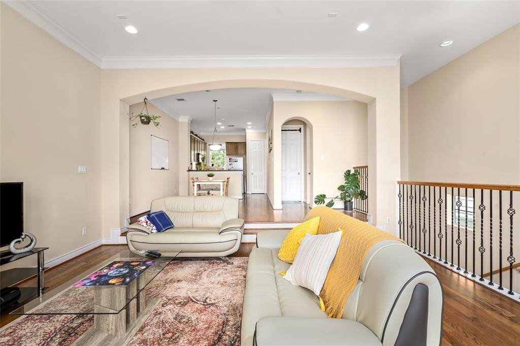 Spacious and inviting, this open-concept living area features beautiful hardwood flooring, high ceilings with recessed lighting, and elegant crown molding. A graceful arched entryway leads to the kitchen and dining area, while the wrought iron railing adds a touch of sophistication. The space is filled with natural light and offers the perfect layout for entertaining or relaxing at home.