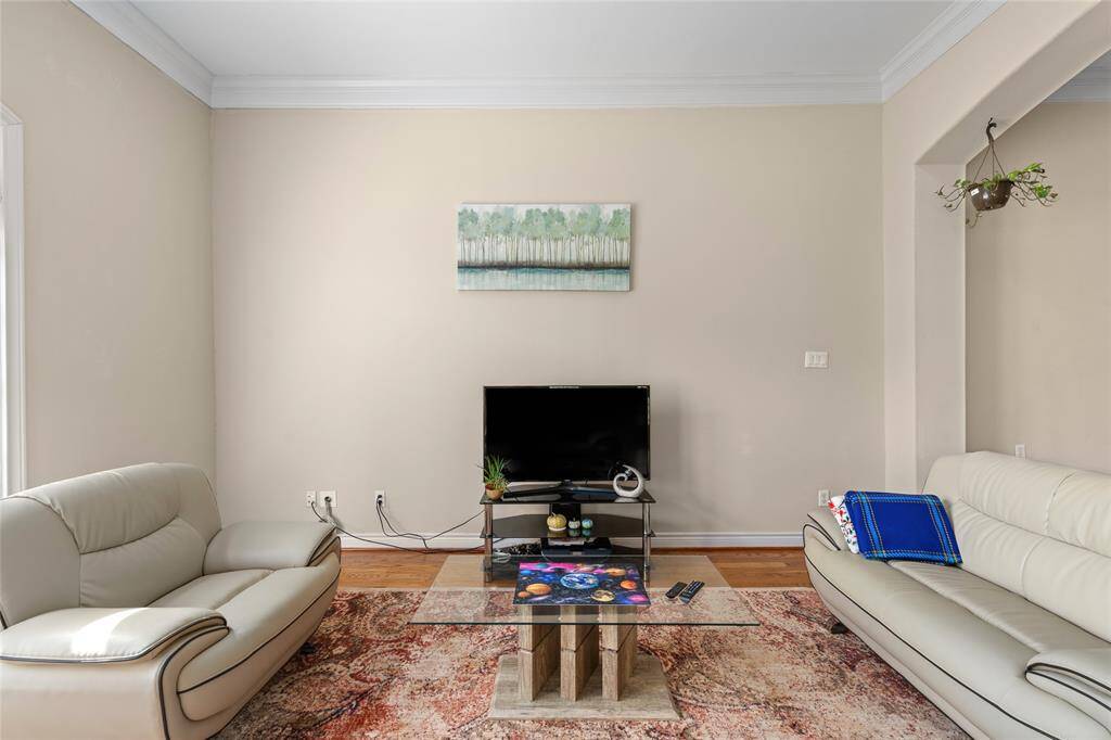 The  living room offers a comfortable, light-filled retreat with neutral tones, crown molding, and warm wood flooring. Its open design seamlessly connects to the dining and kitchen areas, making it ideal for both entertaining guests and enjoying quiet evenings at home.