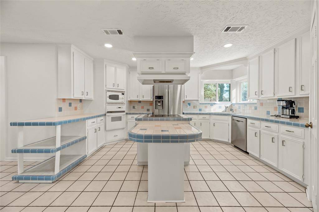 Spacious kitchen features solid wood cabinetry, a central island, and originally built tiles on the countertops and backsplash.