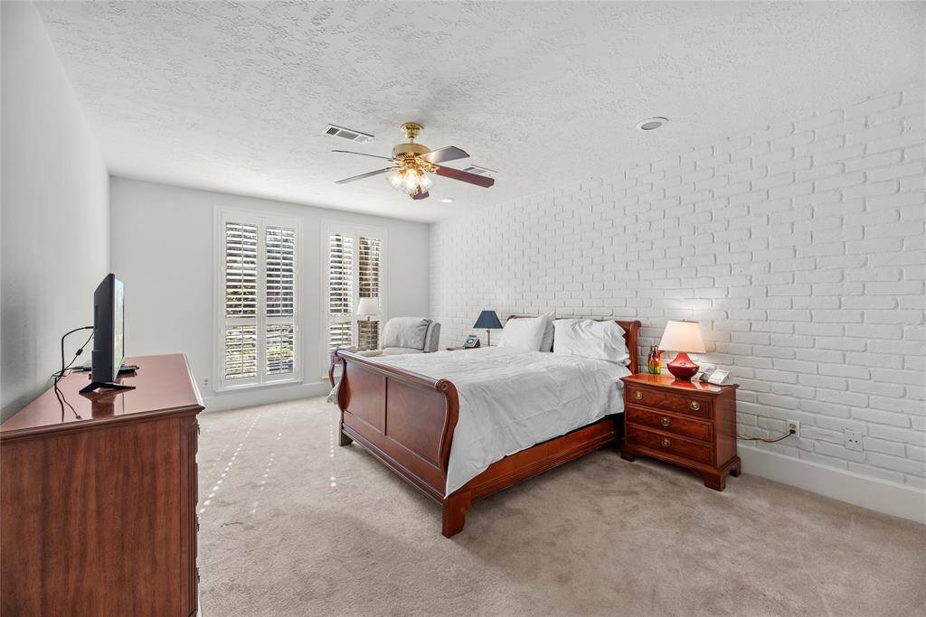 Primary bedroom features plantation style shutters, carpeted floor and a ceiling fan.