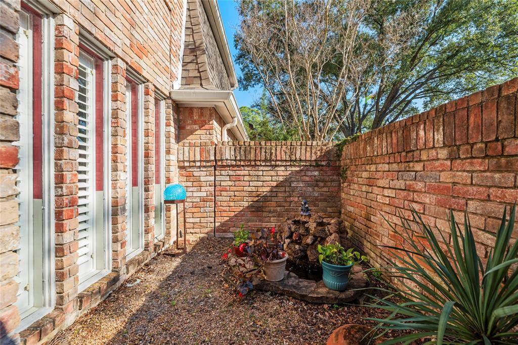 Outdoor front courtyard space features a brick wall, stone patio and a water fountain.