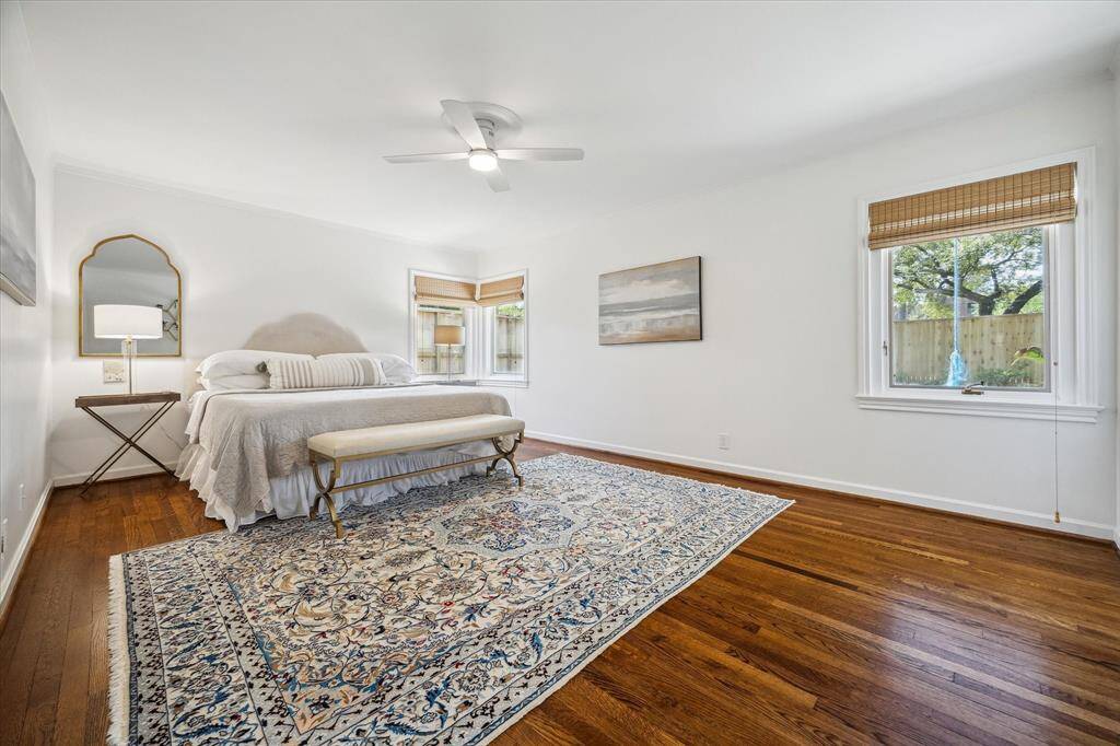 The serene primary suite features rich hardwood floors and a trio of windows framing lush backyard views. Crisp designer paint and a ceiling fan with remote-controlled lighting add to the tranquil atmosphere. A restful retreat tucked quietly away from the main living areas.