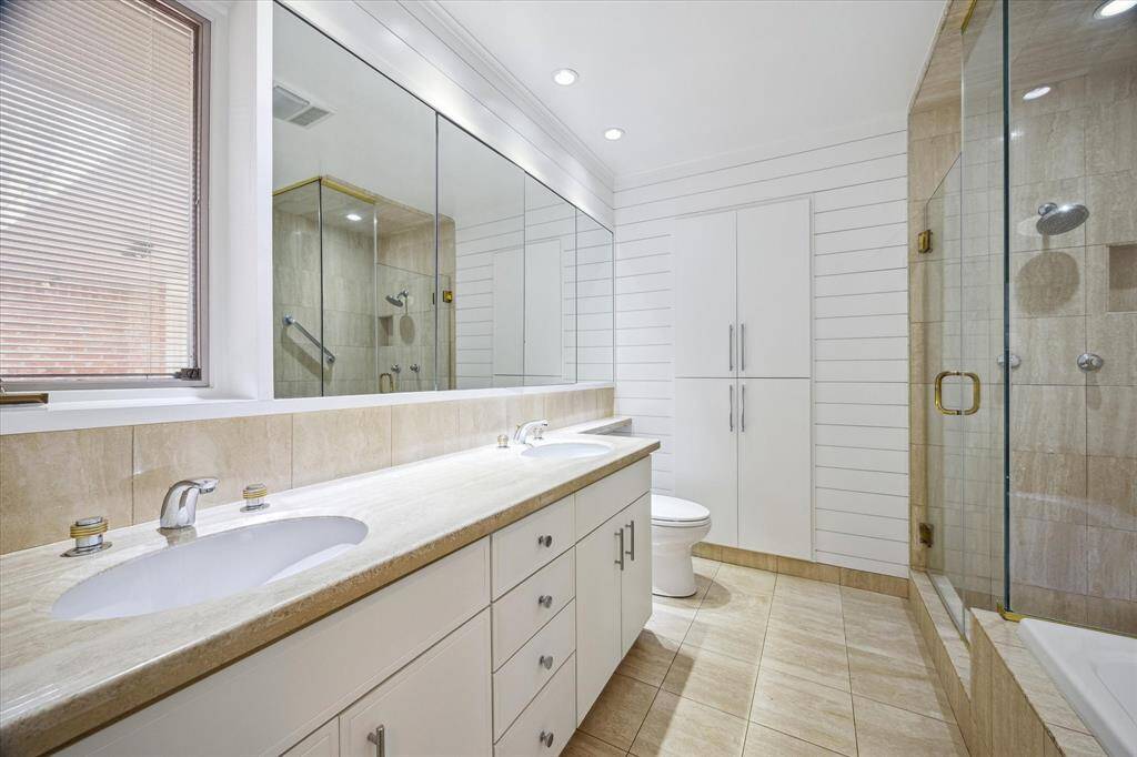 The spa-inspired primary bathroom features dual vanities with travertine countertops, a jetted tub, and a walk-in shower with seamless glass. A large window brings in soft, natural light. Sophisticated yet serene, this space invites daily relaxation.