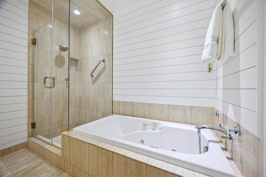 A luxurious Jacuzzi tub sits beside a spacious walk-in shower with seamless glass and polished finishes. Penny gap wall paneling adds a subtle layer of architectural charm. Every element is designed to evoke timeless tranquility.