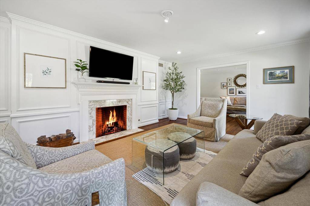 Custom wainscotting and detailed millwork frame this elegant formal living space. A marble-surround fireplace and rich hardwood flooring add timeless sophistication. The room radiates warmth and grandeur for elevated everyday living.