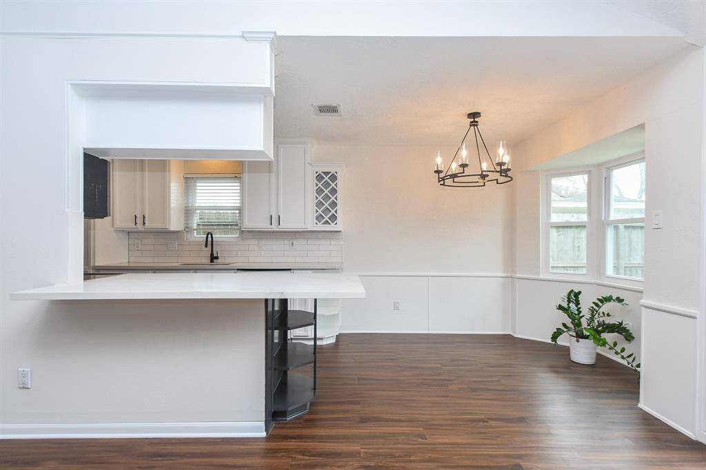 This photo showcases a bright, open kitchen and dining area with modern fixtures. It features white cabinetry, a large pass-through quartz counter, and a stylish chandelier.