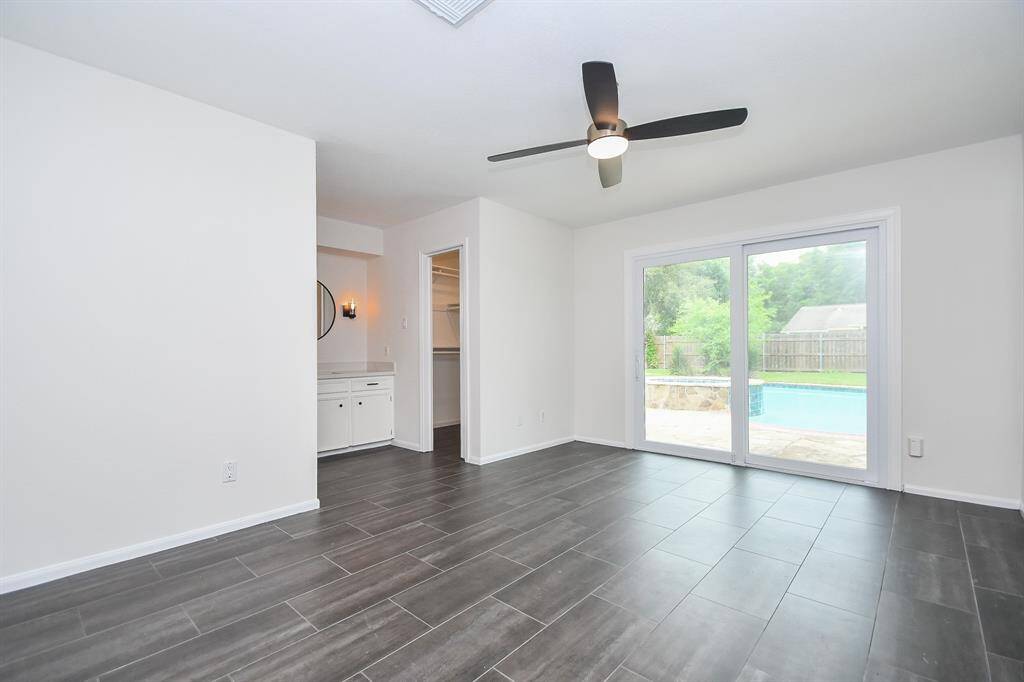 This bright room features sleek dark tile flooring, a modern ceiling fan, and large sliding glass doors leading to a backyard with a pool.