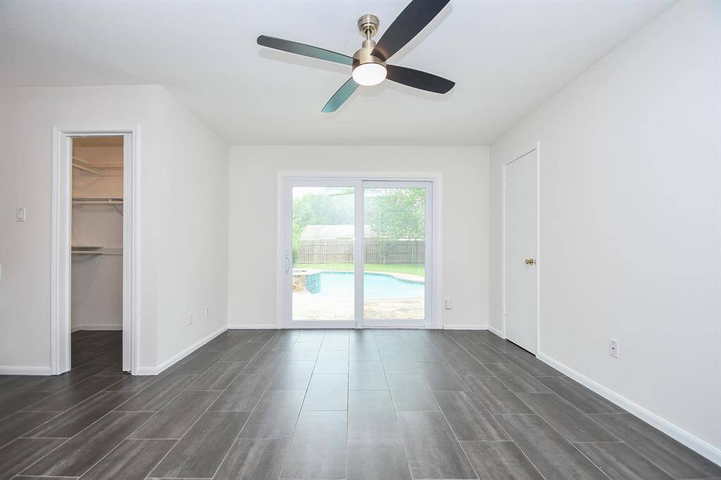 This bright room features sleek dark flooring, a ceiling fan, and sliding glass doors leading to a backyard pool. It includes a walk-in closet and a separate door, offering a spacious and functional layout.