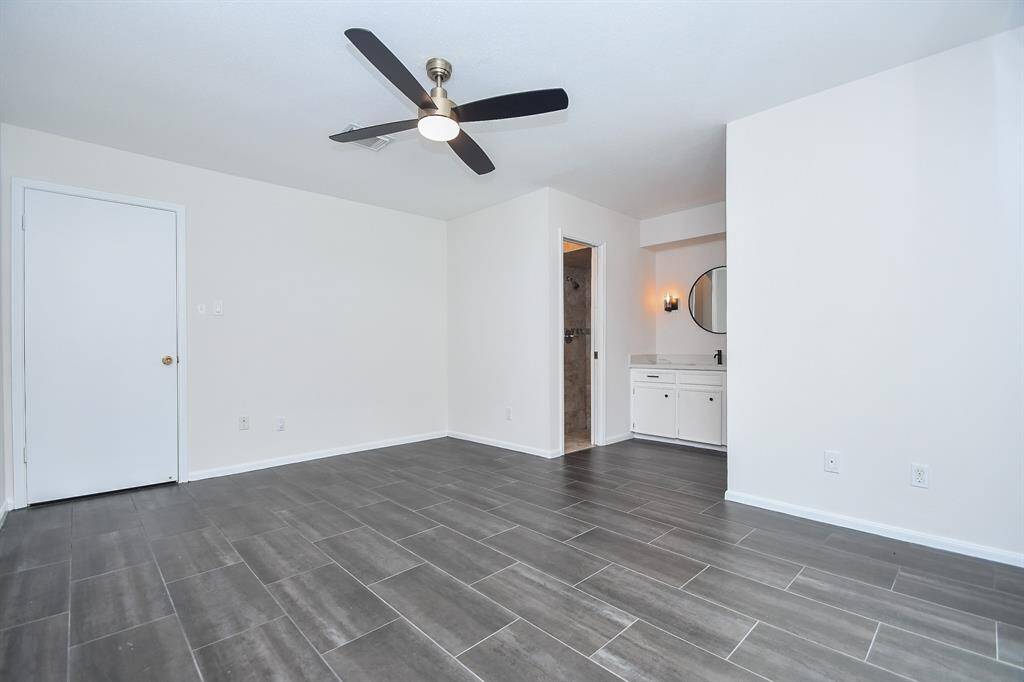 This room features modern gray tile flooring and fresh white walls, equipped with a sleek ceiling fan. It includes an ensuite bathroom with a vanity and mirror, offering a floor to ceiling tiled shower