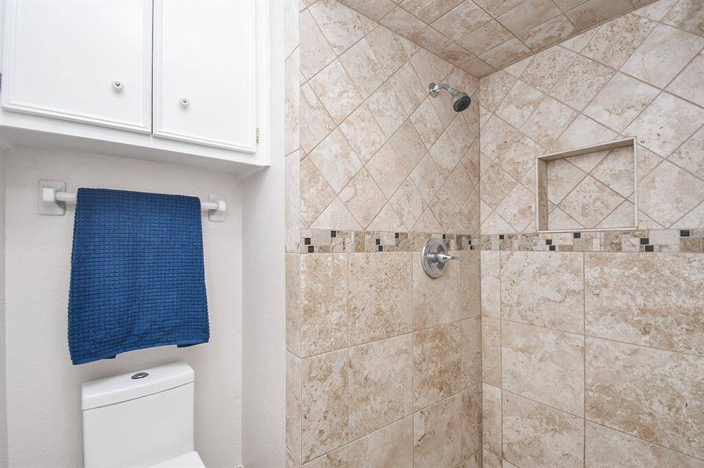 This bathroom features a tiled shower with a built-in niche and decorative border. It includes a modern showerhead and white cabinetry above the toilet.