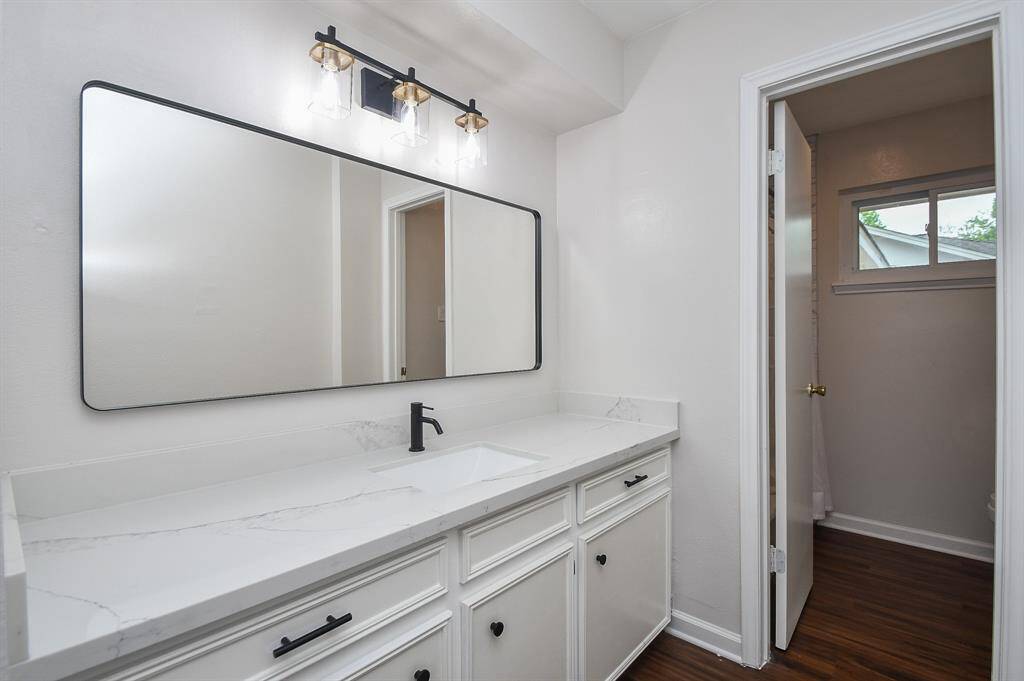 This bathroom features a modern vanity with a sleek quartz countertop an under-mounted sink, complemented by a large rectangular mirror and stylish lighting.