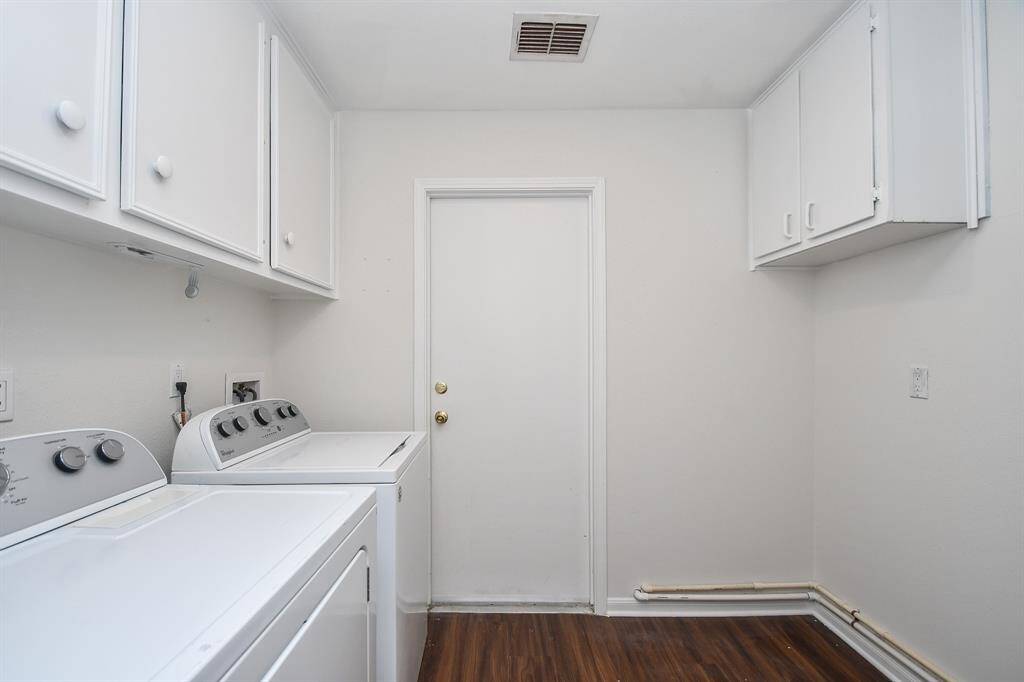 This photo features a clean, functional laundry room, white cabinetry for storage, and waterproof flooring.