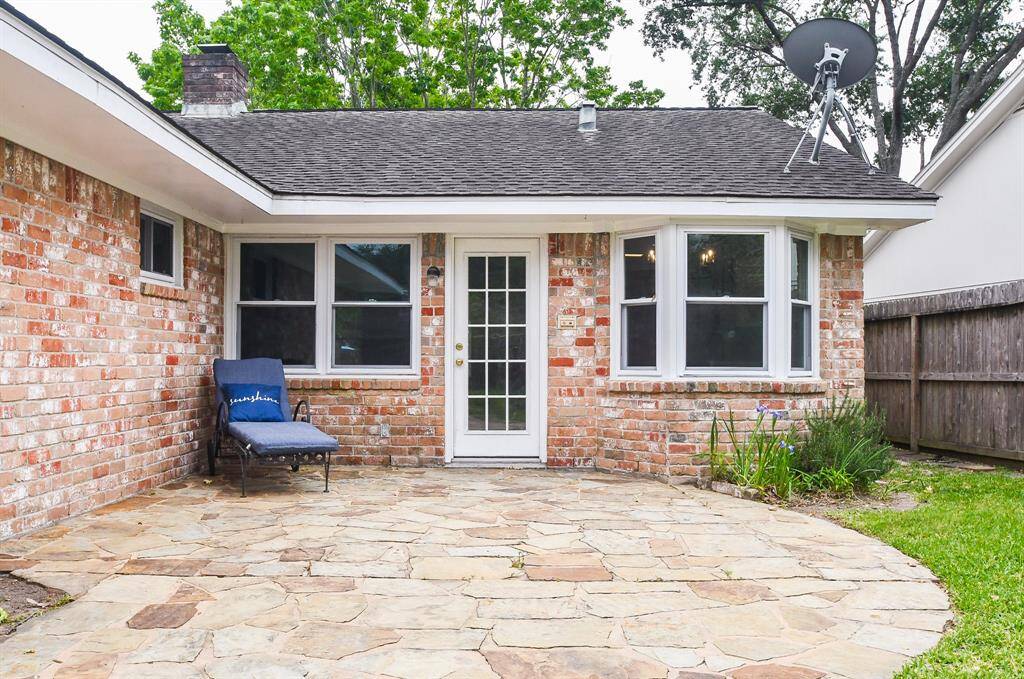Charming brick exterior with a cozy patio area, featuring a stone surface. The space is enclosed by a wooden fence and adorned with simple garden plants, offering a private outdoor retreat.