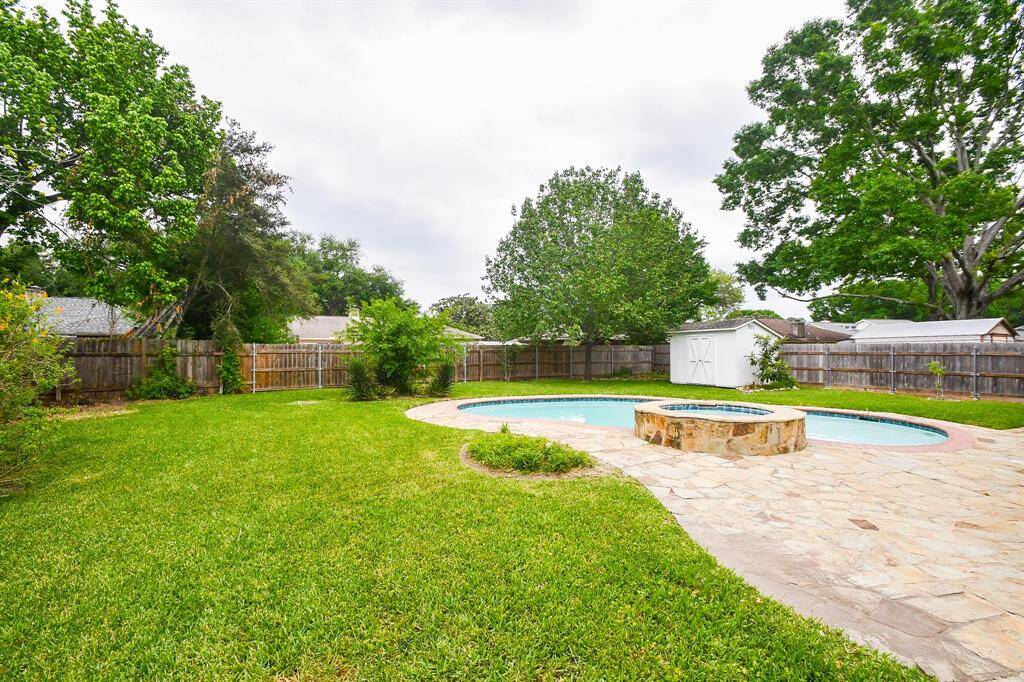 Spacious backyard with a fenced perimeter, featuring a swimming pool and a stone patio. The lush greenery and mature trees provide a serene and private outdoor space, perfect for relaxation and entertainment.
