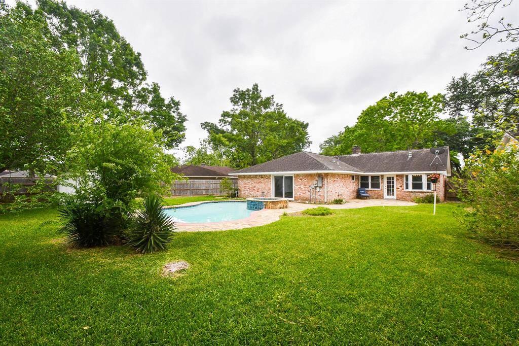 This inviting backyard features a spacious lawn, lush greenery, and a charming in-ground pool, perfect for relaxation and entertaining. The brick exterior of the house adds a classic touch.