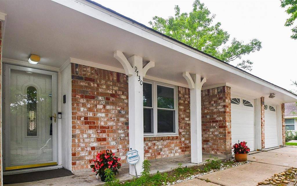This photo showcases the front of a charming brick home with a covered porch supported by decorative white columns. It features a well-maintained front door, a two-car garage, and is accented with potted plants, providing a welcoming curb appeal.