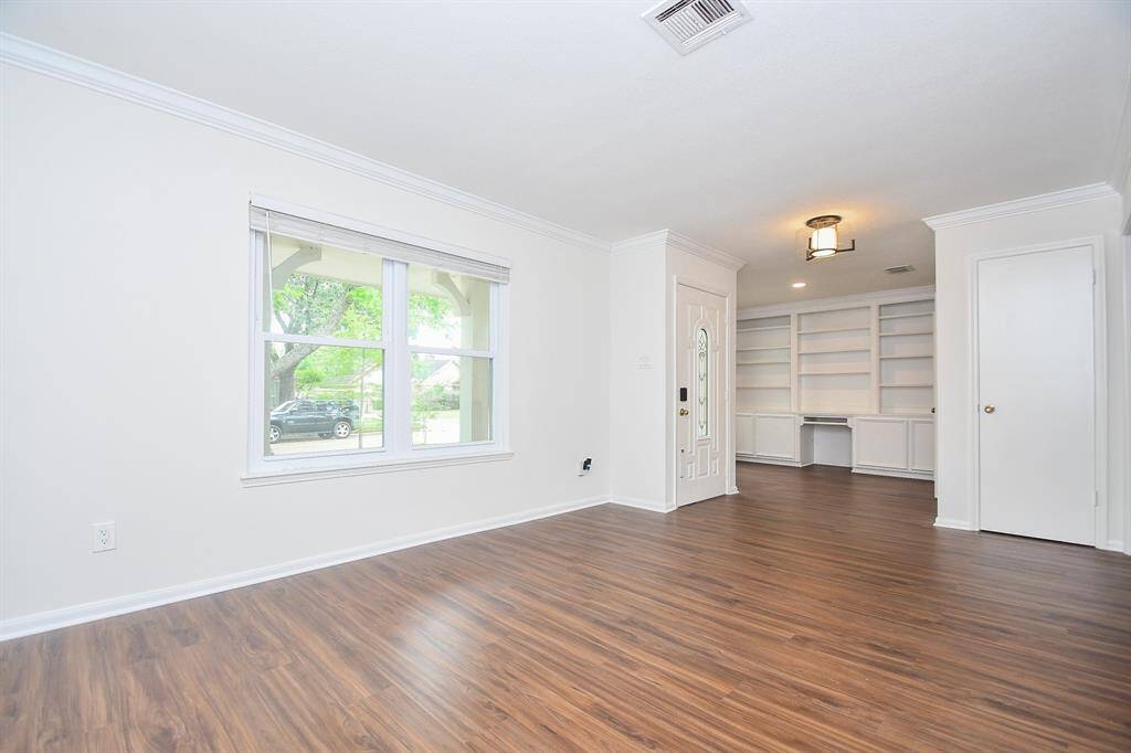 Bright living room with wood look flooring, energy efficient double pane window for natural light, built-in shelving, and a modern light fixture.