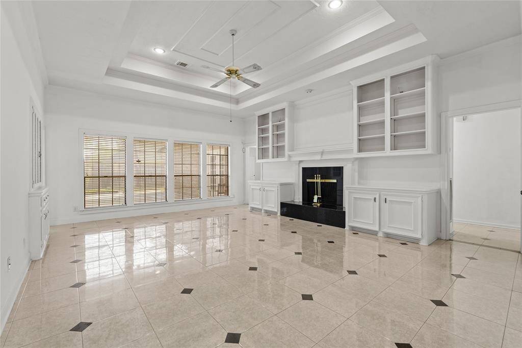 This breathtaking living space is designed to impress with its soaring tray ceiling, elegant recessed lighting, and a stunning wall of windows that fills the room with natural light. The sleek tile flooring enhances the spacious feel, while the built-in cabinetry and grand fireplace create a sophisticated yet inviting focal point. Whether you're hosting family gatherings or enjoying a quiet evening by the fire, this room offers the perfect balance of style and comfort.