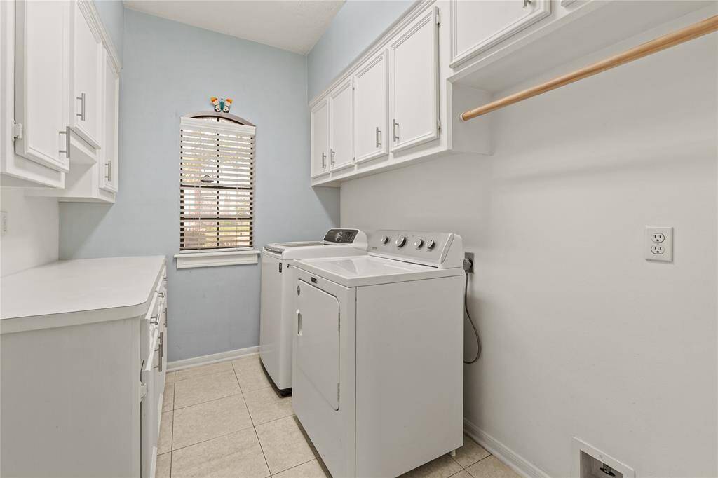 This well-designed laundry room makes household chores feel effortless! With ample cabinetry above and below, there is no shortage of storage for all your essentials. The soft blue accent wall and arched window add a touch of charm, allowing natural light to brighten the space. A convenient countertop provides the perfect spot for folding, while the built-in hanging rod ensures easy organization. The washer and dryer stays.