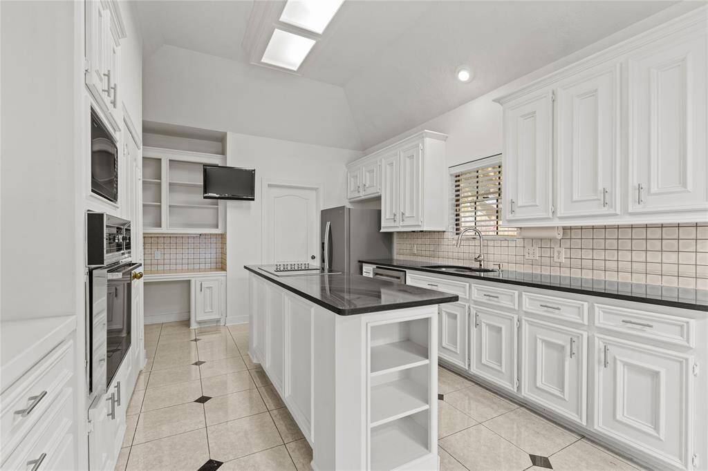 This stunning kitchen is a chef's dream, offering a perfect blend of style and functionality! The sleek black countertops contrast beautifully with the crisp white cabinetry, creating a timeless and elegant design. A spacious island provides additional prep space and storage, while built-in appliances, a deep sink, and a dedicated workstation make meal prep effortless. Skylights and recessed lighting illuminate the space, enhancing its bright and airy feel.