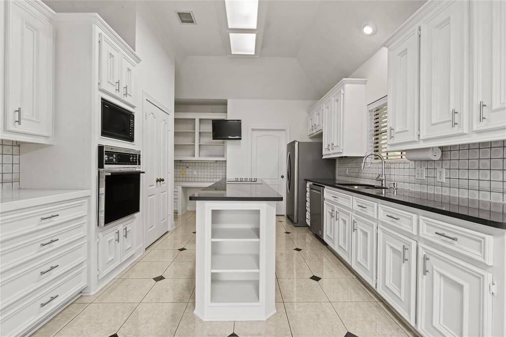 This bright and spacious kitchen is designed to inspire culinary creativity! The pristine white cabinetry provides ample storage space, while the contrasting black granite countertops offer both style and functionality. The island in the center adds even more workspace, perfect for meal prep or casual dining. Skylights flood the room with natural light, enhancing the airy, open feel. With modern appliances, including a built-in oven and sleek refrigerator, this kitchen combines convenience and elegance.